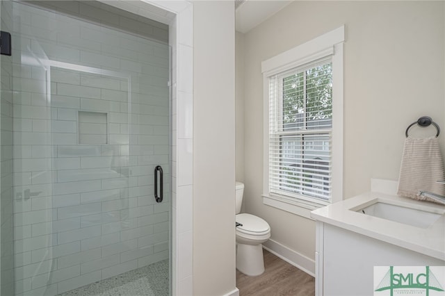 bathroom with baseboards, toilet, vanity, wood finished floors, and a stall shower