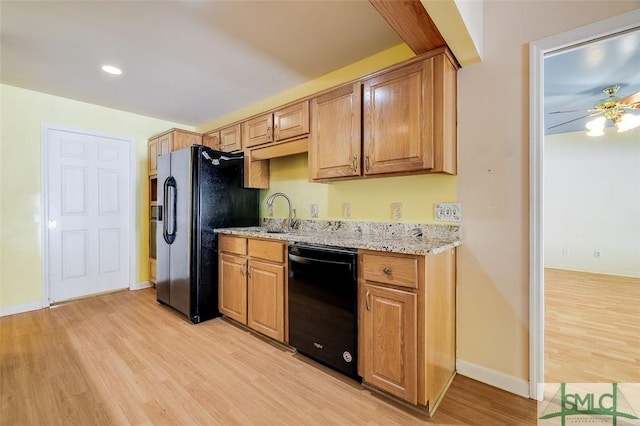 kitchen with baseboards, light stone counters, light wood-style flooring, black appliances, and a sink