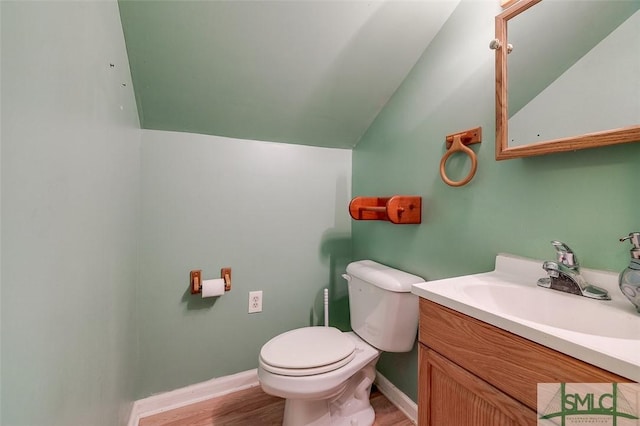 half bathroom featuring vanity, baseboards, toilet, lofted ceiling, and wood finished floors