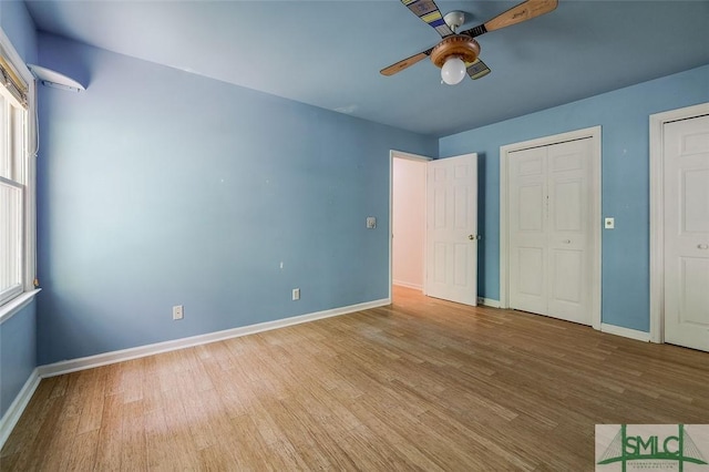 unfurnished bedroom with two closets, wood finished floors, baseboards, and a ceiling fan