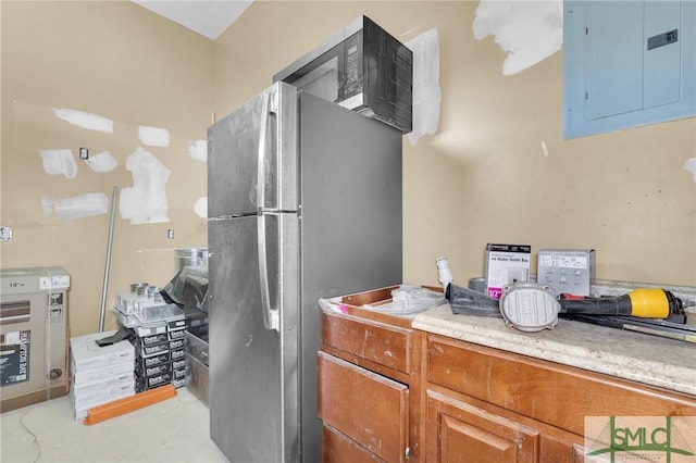 kitchen with electric panel, brown cabinetry, and freestanding refrigerator