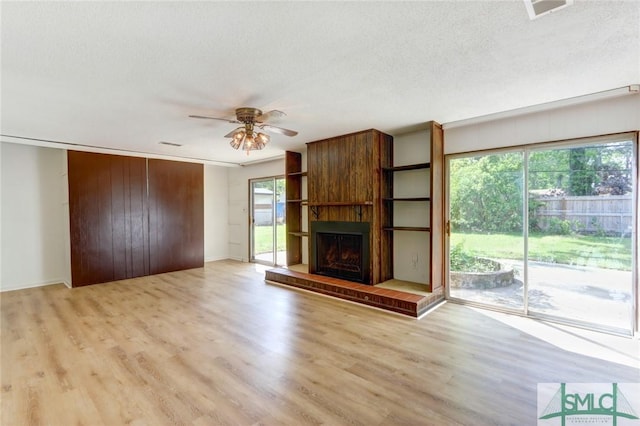 12445 Deerfield Rd, Savannah, GA 31419 - unfurnished living room featuring a large fireplace, light wood-type flooring, a textured ceiling, a ceiling fan, and visible vents