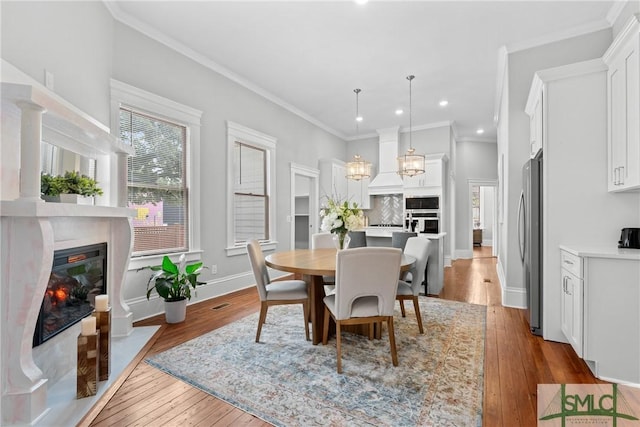 dining area featuring a chandelier, hardwood / wood-style flooring, crown molding, recessed lighting, and a glass covered fireplace