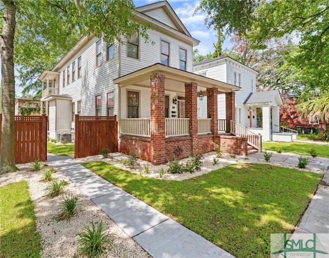 traditional style home featuring brick siding, a porch, fence, and a front lawn