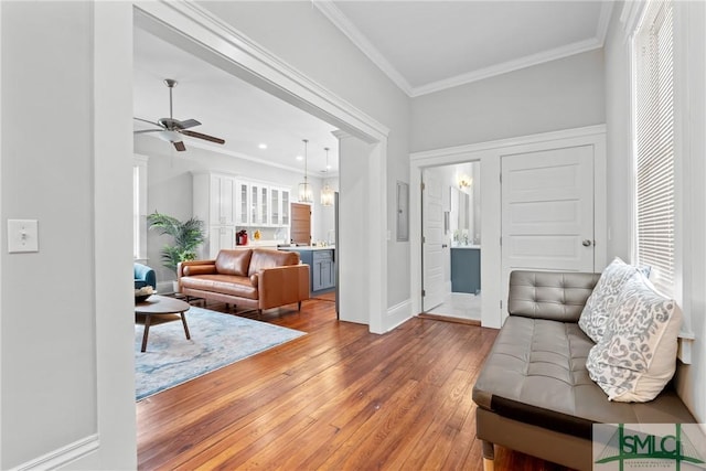 living area featuring crown molding, baseboards, light wood-type flooring, and ceiling fan with notable chandelier