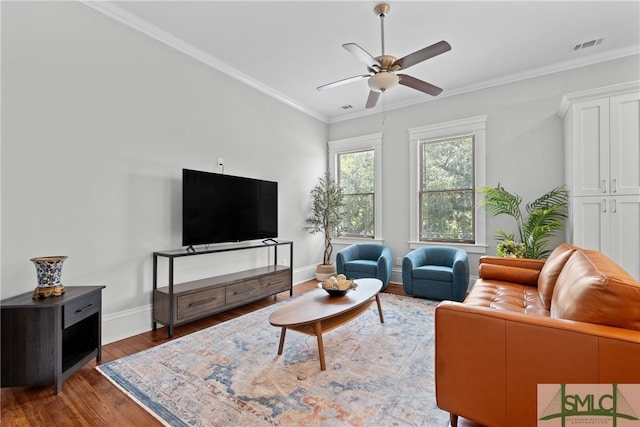 living room featuring ceiling fan, ornamental molding, visible vents, wood finished floors, and baseboards