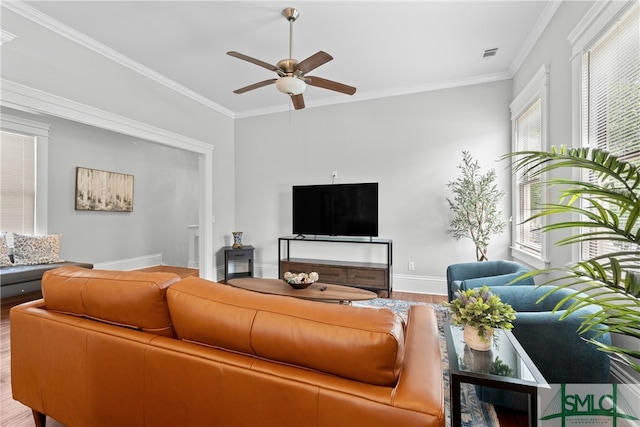 living room featuring baseboards, ornamental molding, visible vents, ceiling fan, and wood finished floors