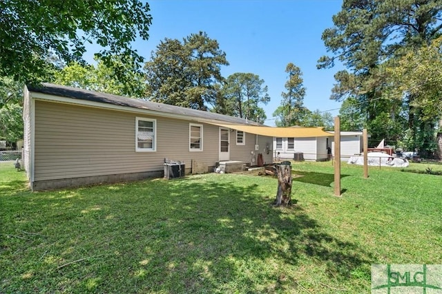 rear view of house with central air condition unit, fence, and a lawn