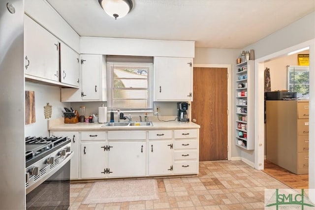 kitchen with white cabinetry, light countertops, a sink, and gas stove