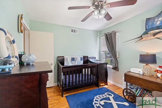 bedroom featuring ceiling fan, a nursery area, visible vents, wood finished floors, and baseboards