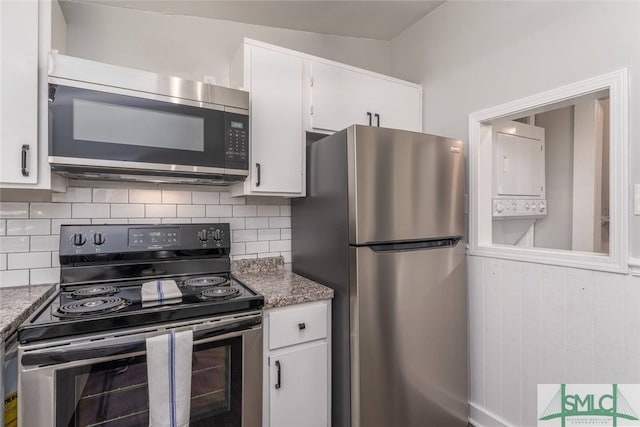 kitchen featuring tasteful backsplash, white cabinets, stacked washer and dryer, stainless steel appliances, and stone countertops
