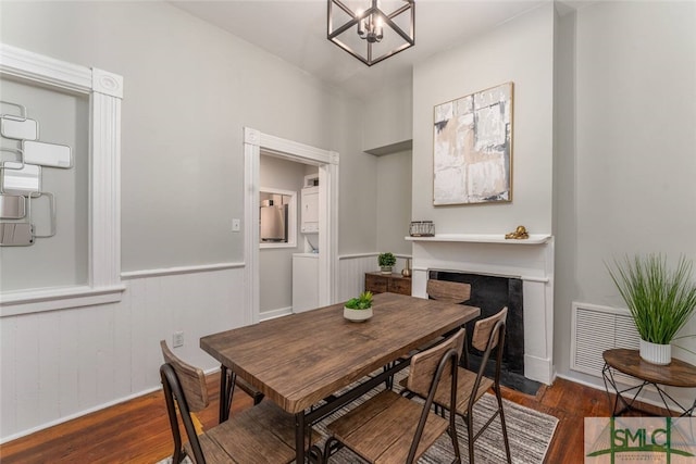 dining room featuring a notable chandelier, a wainscoted wall, a fireplace with flush hearth, visible vents, and wood finished floors