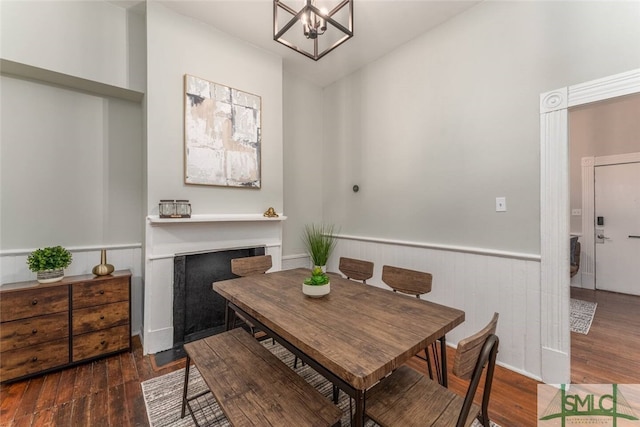 dining space featuring a chandelier, wood finished floors, and a wainscoted wall