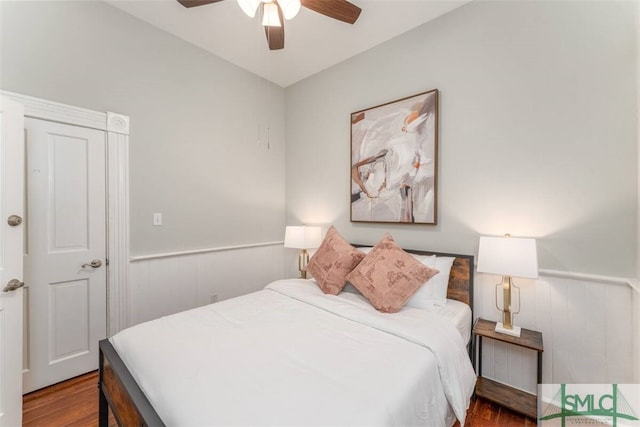 bedroom with wood finished floors, ceiling fan, and a wainscoted wall