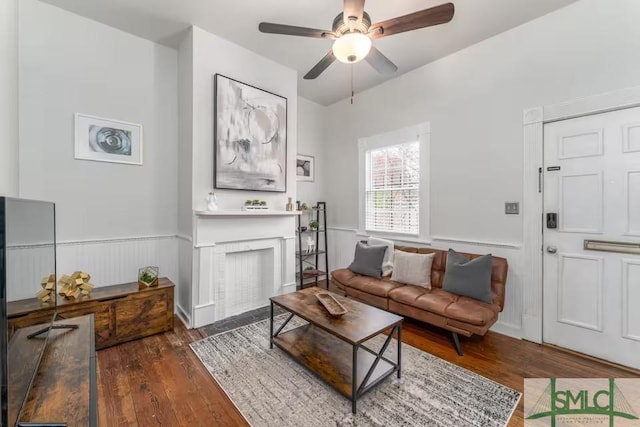 living room with a brick fireplace, a ceiling fan, wainscoting, and hardwood / wood-style flooring