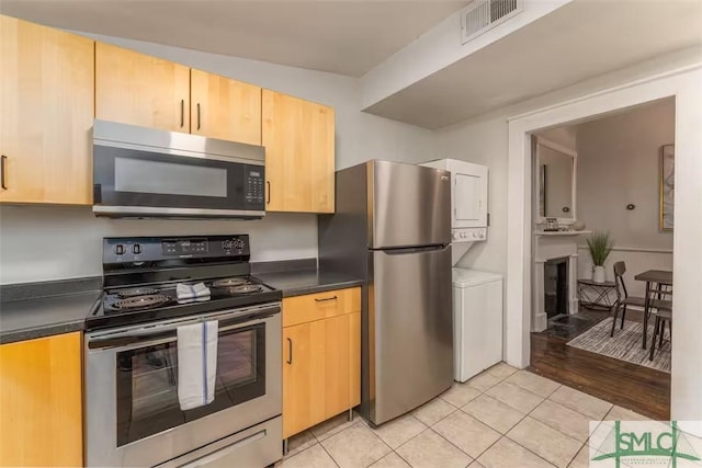 kitchen featuring dark countertops, appliances with stainless steel finishes, stacked washer / drying machine, and visible vents