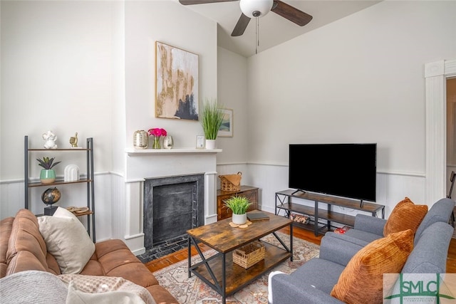 living room featuring a fireplace with flush hearth, wainscoting, lofted ceiling, and ceiling fan