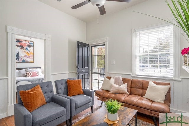 living room featuring wood finished floors, a ceiling fan, and wainscoting