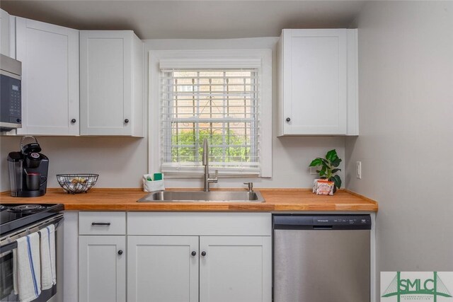 kitchen with butcher block countertops, a sink, white cabinets, and stainless steel appliances