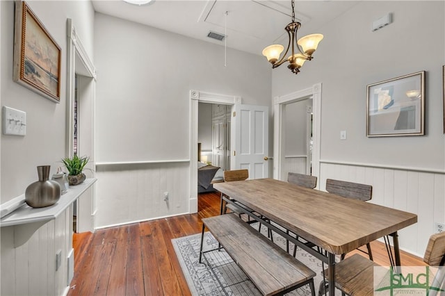 dining space featuring a chandelier, visible vents, wood-type flooring, wainscoting, and attic access