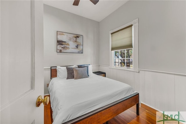 bedroom with ceiling fan, a wainscoted wall, and wood finished floors