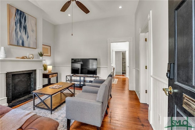 living area with a fireplace with flush hearth, wainscoting, recessed lighting, wood finished floors, and ceiling fan