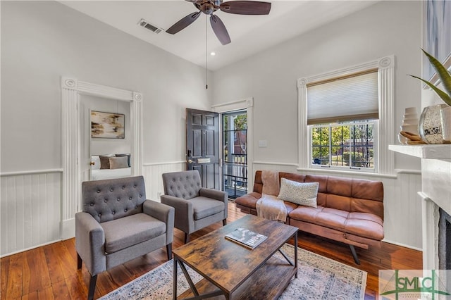 living area with wainscoting, visible vents, ceiling fan, hardwood / wood-style floors, and a fireplace