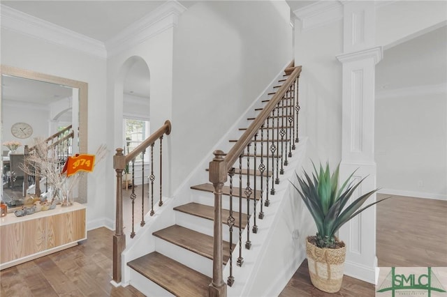 stairway featuring baseboards, ornate columns, ornamental molding, and wood finished floors
