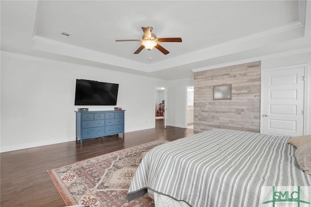 bedroom featuring baseboards, wood finished floors, a tray ceiling, and visible vents