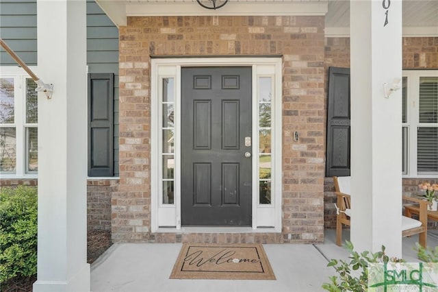 view of exterior entry with a porch and brick siding
