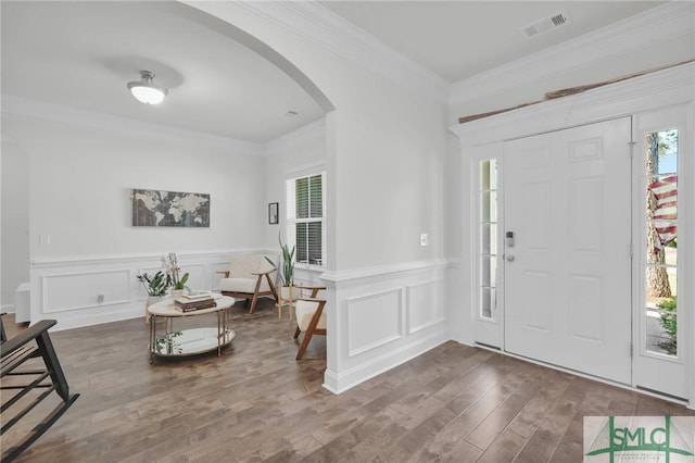 foyer featuring a decorative wall, crown molding, wood finished floors, arched walkways, and visible vents