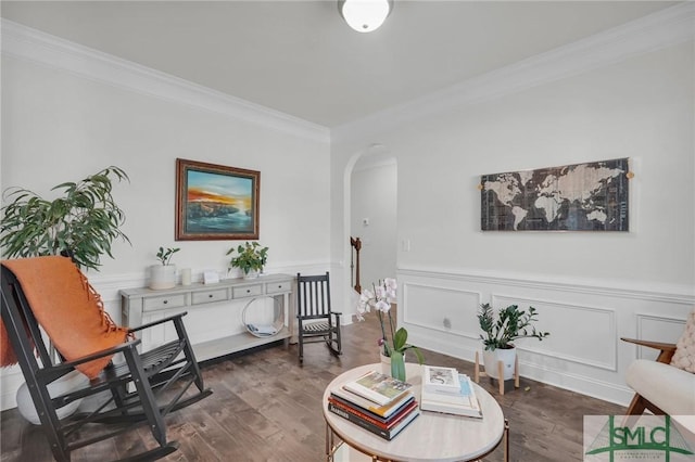 living area featuring arched walkways, dark wood-type flooring, wainscoting, and crown molding