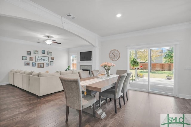 dining room featuring arched walkways, a fireplace, dark wood finished floors, and visible vents