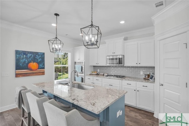 kitchen with a chandelier, an island with sink, dark wood-type flooring, decorative backsplash, and appliances with stainless steel finishes