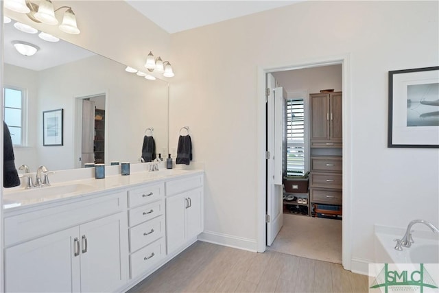 bathroom with wood finished floors, double vanity, a sink, and baseboards