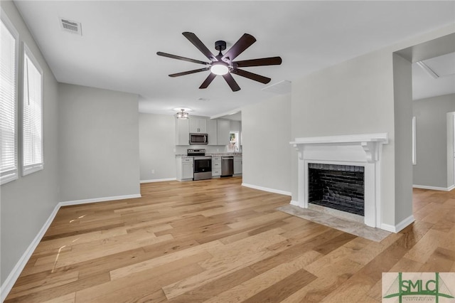 unfurnished living room featuring a ceiling fan, baseboards, a fireplace with flush hearth, light wood-type flooring, and visible vents