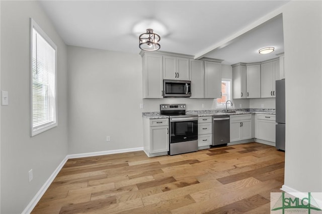 kitchen with appliances with stainless steel finishes, light stone countertops, baseboards, beamed ceiling, and light wood-style flooring