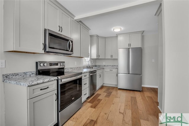 kitchen featuring light stone countertops, appliances with stainless steel finishes, a sink, baseboards, and light wood-type flooring