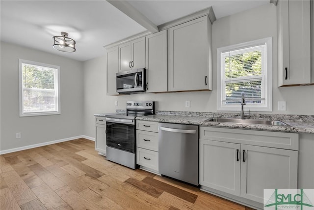 kitchen with baseboards, a sink, light wood-style flooring, and appliances with stainless steel finishes