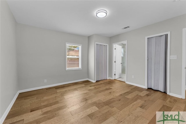 unfurnished bedroom with visible vents, multiple closets, baseboards, and light wood-type flooring
