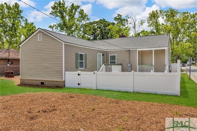 back of property featuring fence, a shingled roof, and a lawn