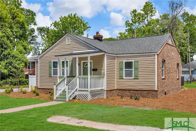 view of front of property with covered porch, a chimney, a front yard, roof with shingles, and brick siding