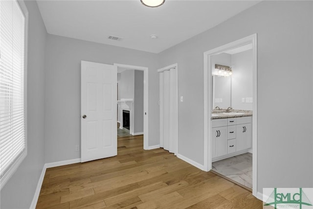 unfurnished bedroom with visible vents, a fireplace, baseboards, light wood-style floors, and ensuite bath