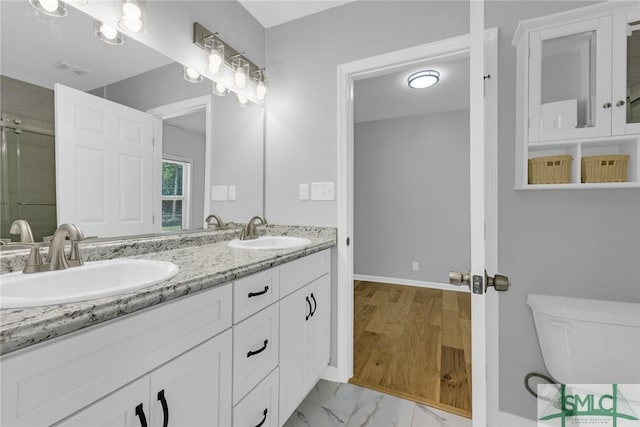 full bath with a sink, a shower with door, toilet, and double vanity