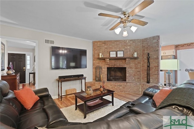 living room featuring a fireplace, crown molding, visible vents, ceiling fan, and wood finished floors