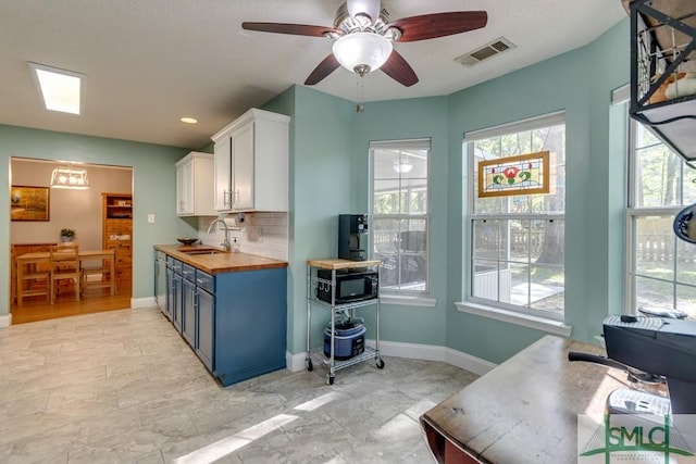 kitchen featuring white cabinets, a sink, tasteful backsplash, visible vents, and butcher block countertops