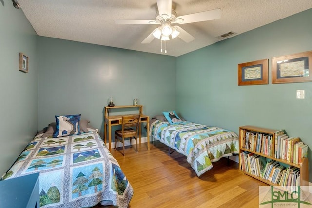 bedroom with wood finished floors, visible vents, a textured ceiling, and a ceiling fan