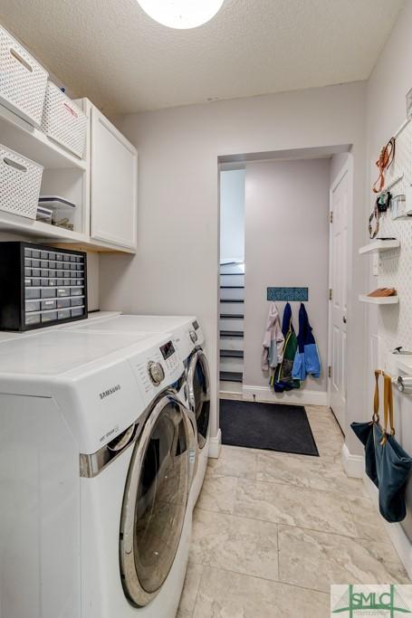 laundry room featuring washing machine and clothes dryer, cabinet space, a textured ceiling, and baseboards