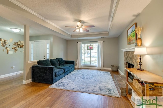 living area featuring a tray ceiling, wood finished floors, crown molding, and ceiling fan