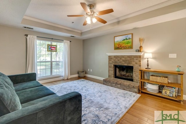 living area with a tray ceiling, visible vents, light wood finished floors, and ornamental molding